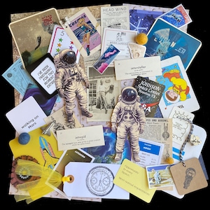 May include: A collage of vintage paper ephemera with a space exploration theme. The collage includes images of astronauts, rockets, planets, and stars. There are also several handwritten notes and drawings. The collage is a mix of colors, including blue, red, yellow, and green.