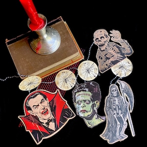 May include: A Halloween garland with a black and white spiderweb design, a black and white illustration of a vampire, a black and white illustration of Frankenstein's monster, a black and white illustration of a skeleton, and a black and white illustration of a zombie.