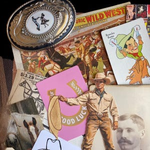 May include: A collection of vintage Western-themed items. Includes a silver belt buckle with a dancing couple, playing cards, a pink card with "GOOD LUCK" text, and a cowboy cutout. The items are arranged on a black surface.