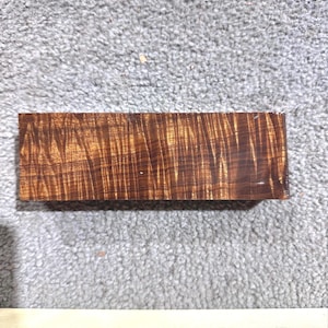 May include: A close-up of a piece of wood with a beautiful, intricate grain pattern. The wood is a rich brown colour with streaks of gold and red. The wood is smooth and polished.
