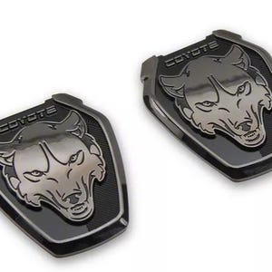 May include: Two black and silver Coyote emblem badges. Each badge features a stylized wolf head with the word "COYOTE" above it. The badges have a textured background and a glossy finish.