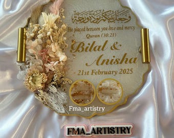 May include: A white and gold resin tray with a gold handle. The tray is decorated with dried flowers and a gold inscription that reads "He placed between you love and mercy Quran (30:21) Bilal & Anisha 21st February 2025".