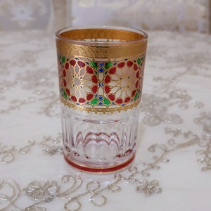 May include: A clear glass drinking glass with a gold rim and intricate red, green, and blue geometric patterns around the middle.