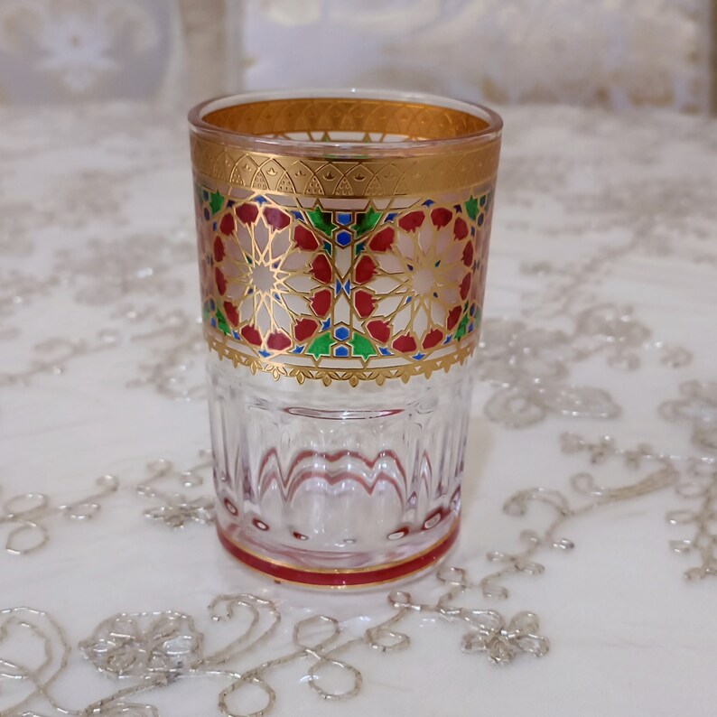 May include: A clear glass drinking glass with a gold rim and intricate red, green, and blue geometric patterns around the middle.