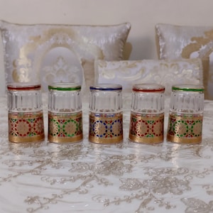 May include: Set of five clear glass shot glasses with gold, red, blue, and green decorative patterns around the middle of each glass.