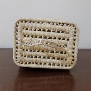 May include: A rectangular woven basket with a handle made of natural straw. The basket has a light beige color and a woven pattern.