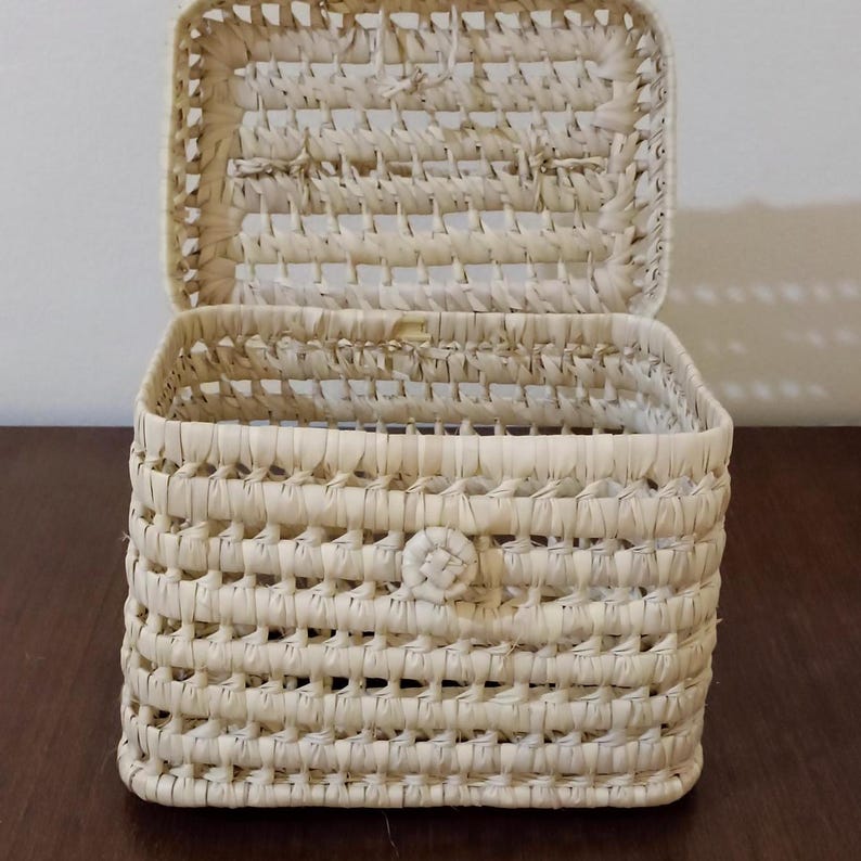 May include: A woven rectangular storage box with a lid. The box is made of natural straw and has a light beige color.