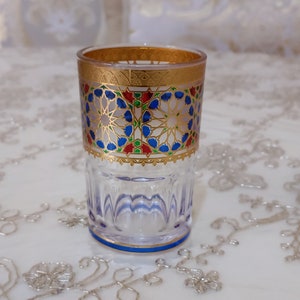 May include: A clear glass drinking glass with a gold rim and intricate blue, red, and green geometric patterns around the middle.