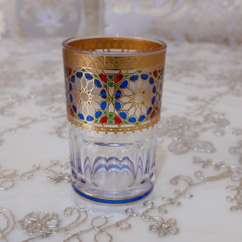 May include: A clear glass drinking glass with a gold rim and intricate blue, red, and green geometric patterns around the middle.