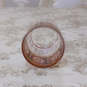 May include: A clear glass tumbler with a colorful, geometric pattern around the rim. The pattern features pink, red, green, and blue colors.