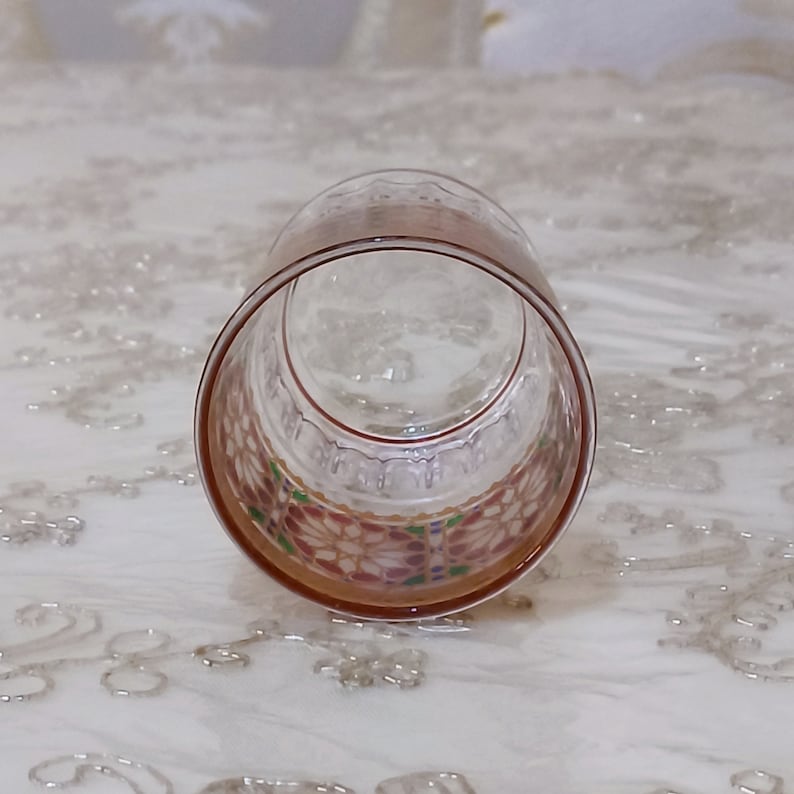 May include: A clear glass tumbler with a colorful, geometric pattern around the rim. The pattern features pink, red, green, and blue colors.