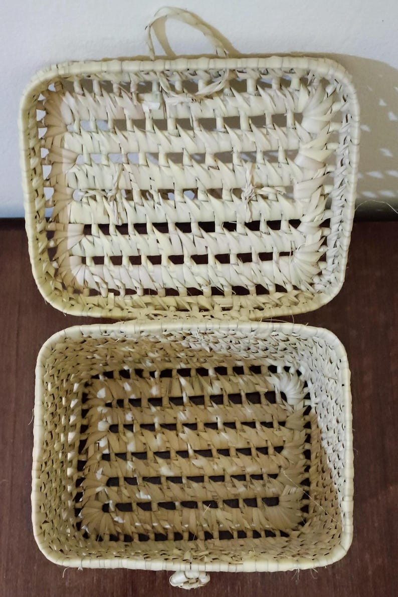 May include: A woven basket with a lid, made of natural materials, with a light beige color. The basket is open and the lid is resting on top.