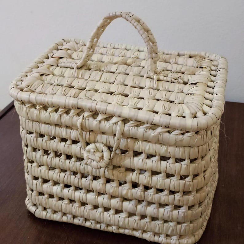 May include: A woven rectangular basket with a handle. The basket is made of natural straw and has a light beige color.