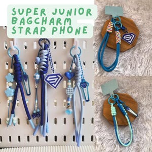 May include: A selection of blue phone charms and straps, featuring decorative beads, charms, and the text "SUPER JUNIOR BAGCHARM STRAP PHONE." Some have a diamond-shaped logo. The straps are attached to key rings.