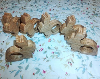 Puede incluir: Seis anillos de servilleta de madera con forma de conejo. Los anillos son de madera marrón claro y tienen un acabado natural.