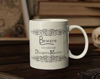 May include: White ceramic mug with a black and white design. The mug features a decorative border and the text "Beware the smiling Dungeon Master".