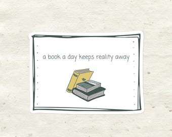 Puede incluir: Una pegatina blanca con bordes negros y el texto "a book a day keeps reality away." Una pila de libros está ilustrada en el centro de la pegatina. El libro de arriba es amarillo, y los dos libros de abajo son verdes y negros.