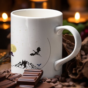 May include: White ceramic mug with a black and white illustration of a castle, mountains, a moon, and three dragons. The mug is surrounded by chocolate pieces and chocolate chips.