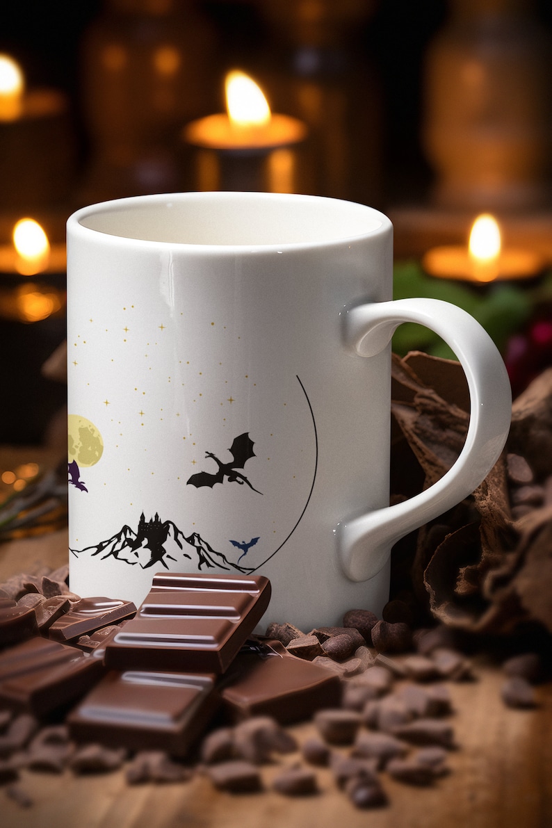 May include: White ceramic mug with a black and white illustration of a castle, mountains, a moon, and three dragons. The mug is surrounded by chocolate pieces and chocolate chips.