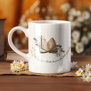 May include: White ceramic mug with a curved handle, decorated with an open book illustration, floral accents, and the text "books became my best friends." Daisies and a book are in the background.