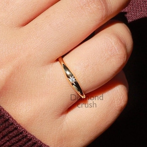 May include: A thin gold band ring with a single small diamond set in the centre.