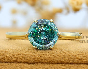 May include: A gold ring with a large, round, teal gemstone. The ring is set on a brown surface with a blurred background of dried flowers. The text "Diamond crush" is visible on the right side.