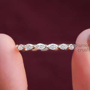 May include: A delicate gold band ring with a row of marquise-shaped diamonds. The ring is on a finger.