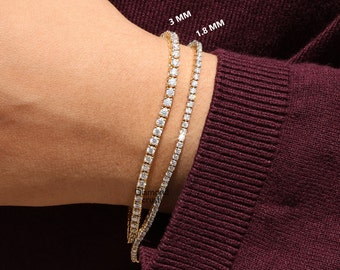 May include: Two gold tennis bracelets with a row of clear diamonds. The bracelet on the left is 3 mm wide and the bracelet on the right is 1.8 mm wide.