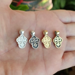 Può includere: Quattro piccoli pendenti a croce ornati in tonalità argento e oro. Ogni pendente presenta un design dettagliato con un anello nella parte superiore per una catena. Le croci sono tenute in una mano.