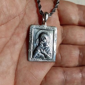 May include: Silver pendant necklace with a religious icon of the Virgin Mary and baby Jesus. The pendant is rectangular and features the inscription "Богородица" in Cyrillic script.