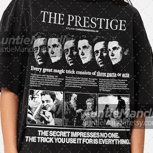 May include: Black t-shirt featuring the movie title "The Prestige" with a film still graphic. The shirt includes text about magic tricks and the phrase "The secret impresses no one. The trick you use it for is everything."
