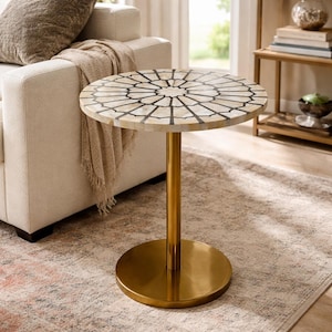 May include: A round side table featuring a tabletop with a white and cream-colored inlaid mosaic pattern in a radial design separated by thin black lines. The table has a single cylindrical gold-toned metal pedestal base and a flat circular base.