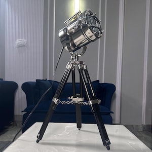May include: A silver spotlight lamp with a black tripod stand. The lamp is on a white table.