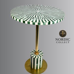 May include: A round side table with a green and white striped top and base. The table has a gold-colored stem and base. The table is 24 inches tall and the top is 18 inches in diameter. The table is from Nordic Collect.