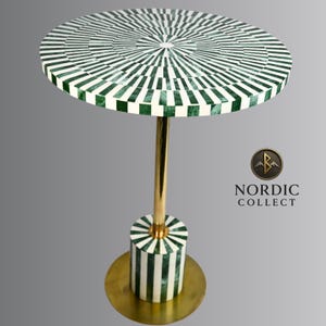 May include: A round side table with a green and white geometric pattern on the tabletop. The table has a gold-colored metal stem and base. The base is cylindrical with matching green and white stripes. The table is approximately 24 inches in diameter.
