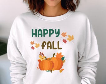 Könnte beinhalten: Weißer Pullover mit dem Text "Happy Fall" in grüner und brauner Schrift. Der Pullover hat ein Motiv aus zwei orangefarbenen Kürbissen mit grünen Blättern und braunen Stielen.
