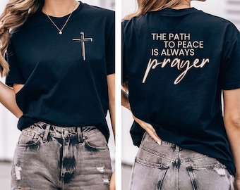 Könnte beinhalten: Schwarzes T-Shirt mit einem Kreuz auf der Vorderseite und dem Text "The path to peace is always prayer" auf der Rückseite.