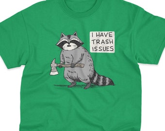 May include: A bright green short-sleeve t-shirt featuring a graphic illustration of a gray raccoon holding a small axe. Next to the raccoon is a white speech bubble containing the black text "I HAVE TRASH ISSUES". The shirt has a crew neckline.