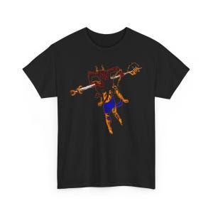 May include: Black t-shirt with a graphic print of a red and orange creature holding a sword. The creature has a blue and white patterned loincloth.