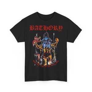 May include: Black t-shirt featuring a red "Bathory" logo and a graphic of a goat-like figure with a blue face and red horns. The text "Under The Sign Of The Black Mark" is printed below the graphic.