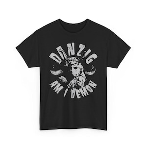 May include: Black t-shirt with a white graphic. The graphic features the word "DANZIG" in a circular design, surrounding a detailed illustration of a figure with horns and the words "AM I DEMON".