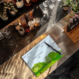 May include: A white cutting board with a green and blue nature scene design. The cutting board has the text "Overlay Mockup PNG" repeated across the surface. A black knife is lying on the cutting board.