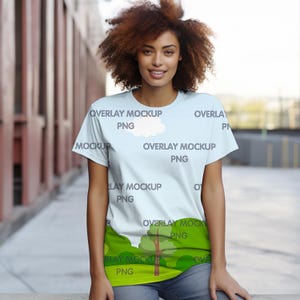 May include: A light blue t-shirt with a white cloud and green trees printed on it. The text "OVERLAY MOCKUP PNG" is repeated on the shirt.