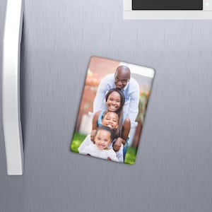 May include: Rectangular family photo magnet featuring a smiling family of five. The magnet is attached to a silver refrigerator door. The family is arranged in a vertical line, with the youngest child in front.