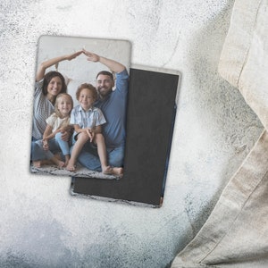 May include: Rectangular photo magnet featuring a family portrait. The image shows a family of four, with the parents forming a roof over their children. The magnet has a black backing and a white border, resting on a textured surface.