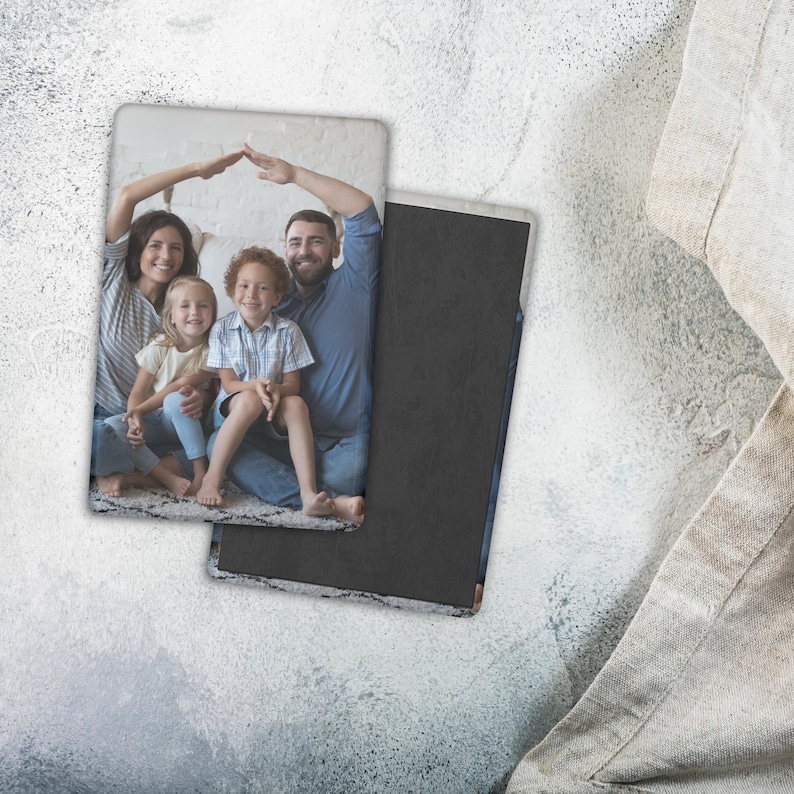 May include: Rectangular photo magnet featuring a family portrait. The image shows a family of four, with the parents forming a roof over their children. The magnet has a black backing and a white border, resting on a textured surface.