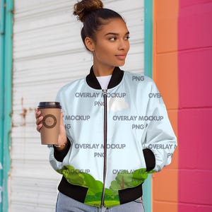 May include: A light blue bomber jacket with a black zipper and black ribbed cuffs. The jacket has a white cloud and green trees printed on it. The text "OVERLAY MOCKUP PNG" is repeated on the jacket.