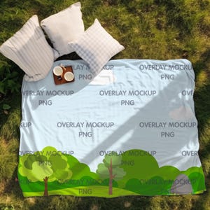 May include: A light blue picnic blanket with a green and white cartoon landscape design. The blanket has the text "Overlay Mockup PNG" repeated throughout the design.