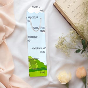 May include: A white and blue bookmark with a green landscape design. The bookmark has a metal clip at the top and the words "OVERLAY MOCKUP PNG" are printed on it.