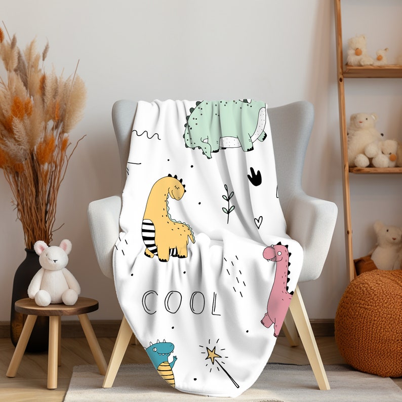 Pu&ograve; includere: Coperta bianca con un motivo di dinosauro colorato. La coperta presenta un dinosauro verde, giallo e rosa con la parola "COOL" stampata su di essa.